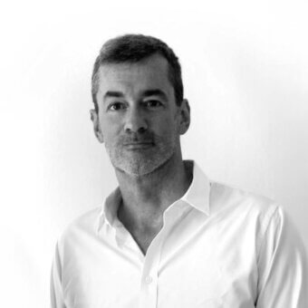 Man portrait, black and white photography, short hair, goatee, white button-down shirt, neutral expression, plain white background, diffused lighting.