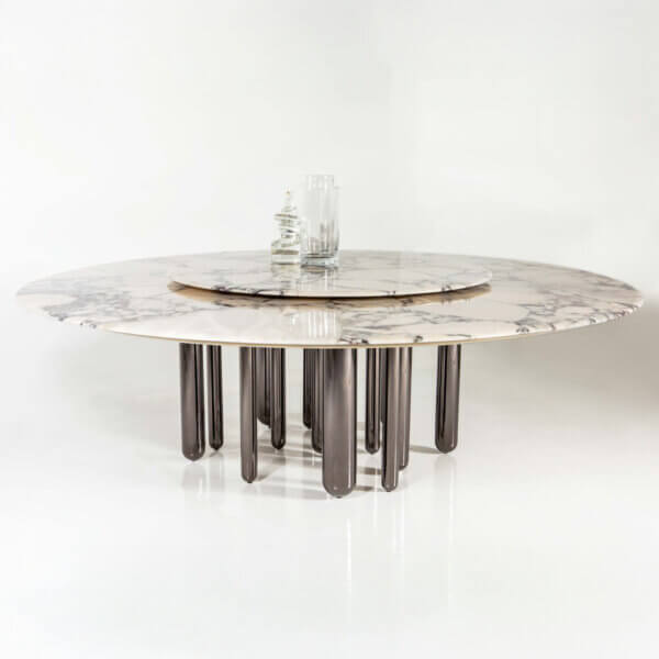 Marble dining table with gray veining, eleven dark gray cylindrical legs, and clear glass vases centered on polished white floor.