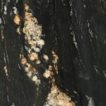 Magma black marble close-up displays swirling patterns with creamy white and golden-tan inclusions, exhibiting a matte, granular stone texture.