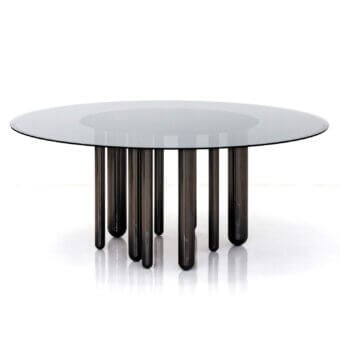Discoteca dining table, glass and gray metal, features a circular glass top supported by nine tapered cylindrical legs.