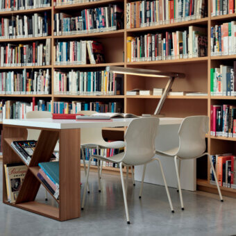 Casamania Stereo chair, white molded plastic, angular design with metal base, studio setting with bookshelf and desk.