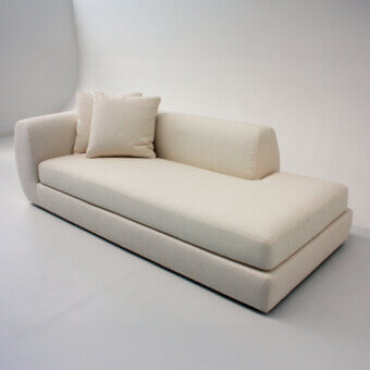 Psyche sofa, beige fabric upholstery, low profile design with curved backrest and boxy armrest, two square cushions, rectangular base.