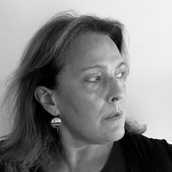 Black and white portrait of Eliana Gerotto, three-quarter profile, dark hair, black top, circular earring, soft lighting, introspective expression.
