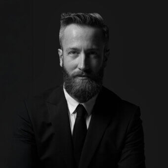 Portrait of Vicente Garcia Jimenez in a black suit, white shirt, and black tie, featuring a gray beard and dark gray background.