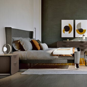 Turri Milano bed, dark gray upholstery, tall headboard with gray & mustard pillows, dark wood frame, linen duvet, abstract art backdrop.