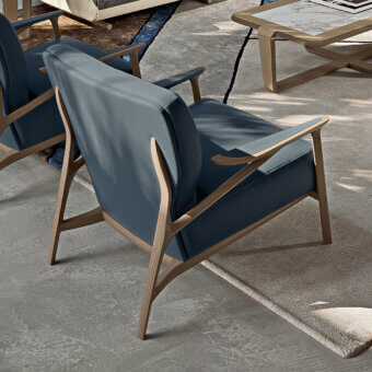Turri Vine lounge chair, teal fabric upholstery, light wood frame with curved armrests, set in a modern gray stone interior.