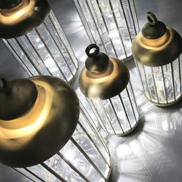 Italamp lanterns, silver metal ribbed cylinders with polished brass caps, studio shot on reflective gray surface, new collection lighting.