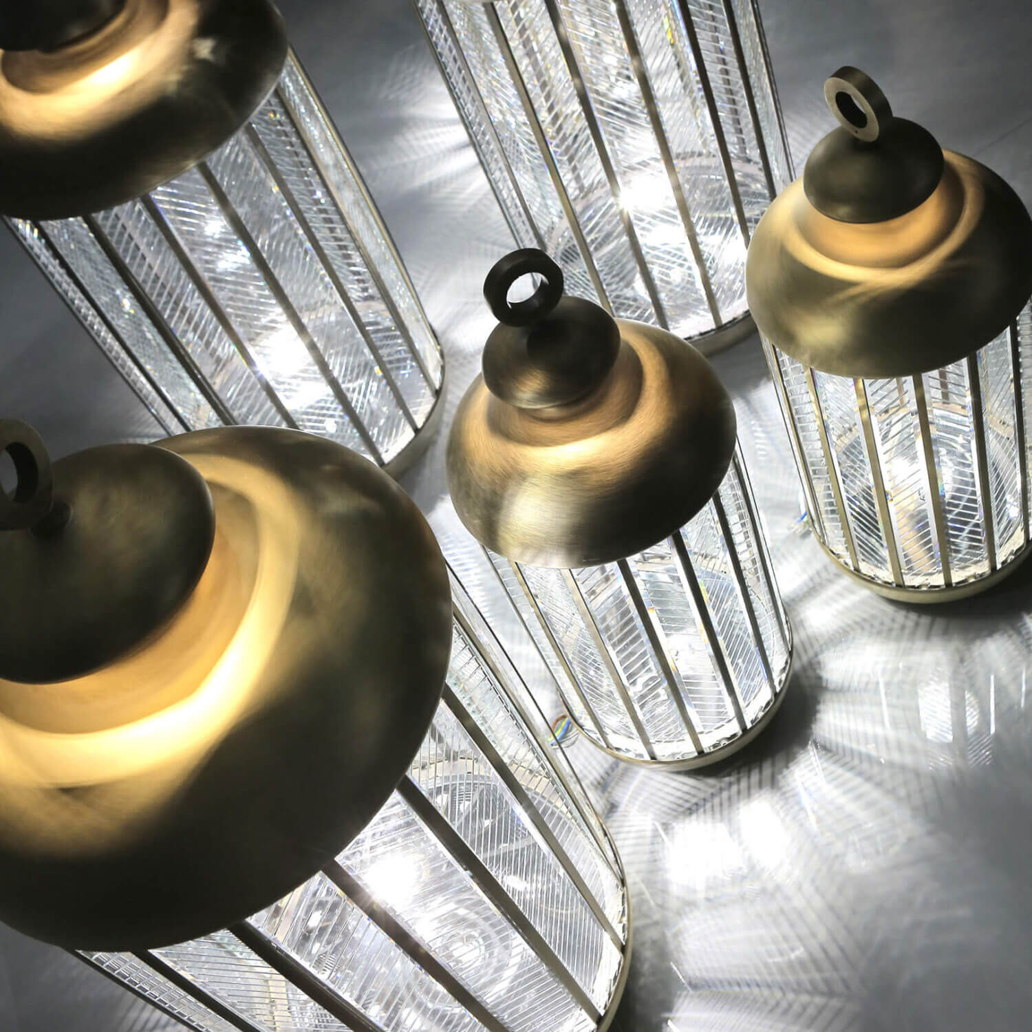 Italamp lanterns, silver metal ribbed cylinders with polished brass caps, studio shot on reflective gray surface, new collection lighting.