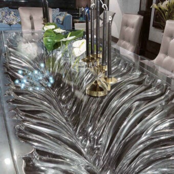 Belmondo Ficus dining table, silver resin wave top, with brass candle holders and white calla lilies, surrounded by dark wood chairs.