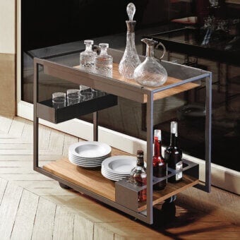 Cattelan Italia mojito wood trolley with two glass shelves, dark metal frame, displaying crystal glassware, porcelain plates, and liquor bottles.