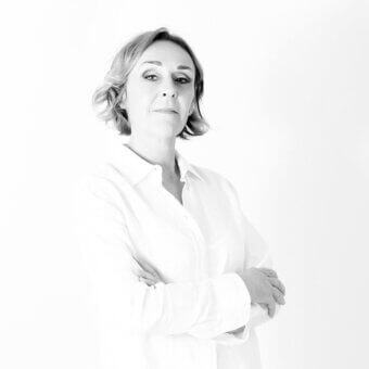 Black and white portrait of Mariateresa Casarola wearing a white shirt, arms crossed, with short layered hair and a neutral expression.