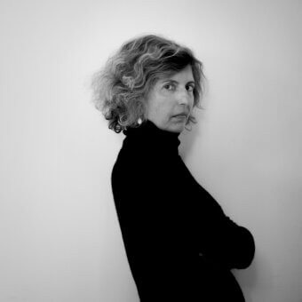 Black and white portrait of Teresa Sapey, a woman with textured hair wearing a black turtleneck, arms crossed, direct gaze.