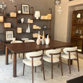 Pacini&Cappellini gio table, dark brown wood top, tapered legs, with six beige upholstered chairs, walnut frames, and spherical glass pendants.