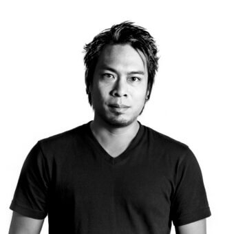 Black and white portrait of dai sugasawa, a man with dark layered hair wearing a black v-neck t-shirt, centered on a white background.