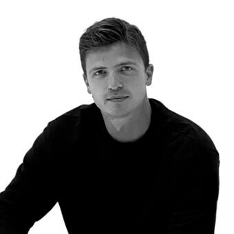 Black and white portrait of Marco Oggian, wearing a dark crew neck shirt, with textured hair and a subtle expression against a white background.