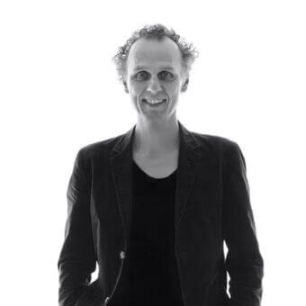 Black and white portrait of Richard Hutten, smiling, wearing a black tank top and textured dark blazer with one button.