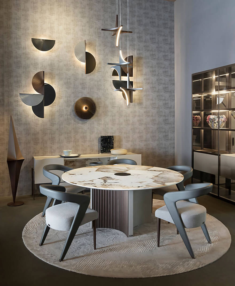 Round dining table with gray metal base, marble-effect top in gray, beige, and white, surrounded by four gray upholstered dining chairs on a rug.