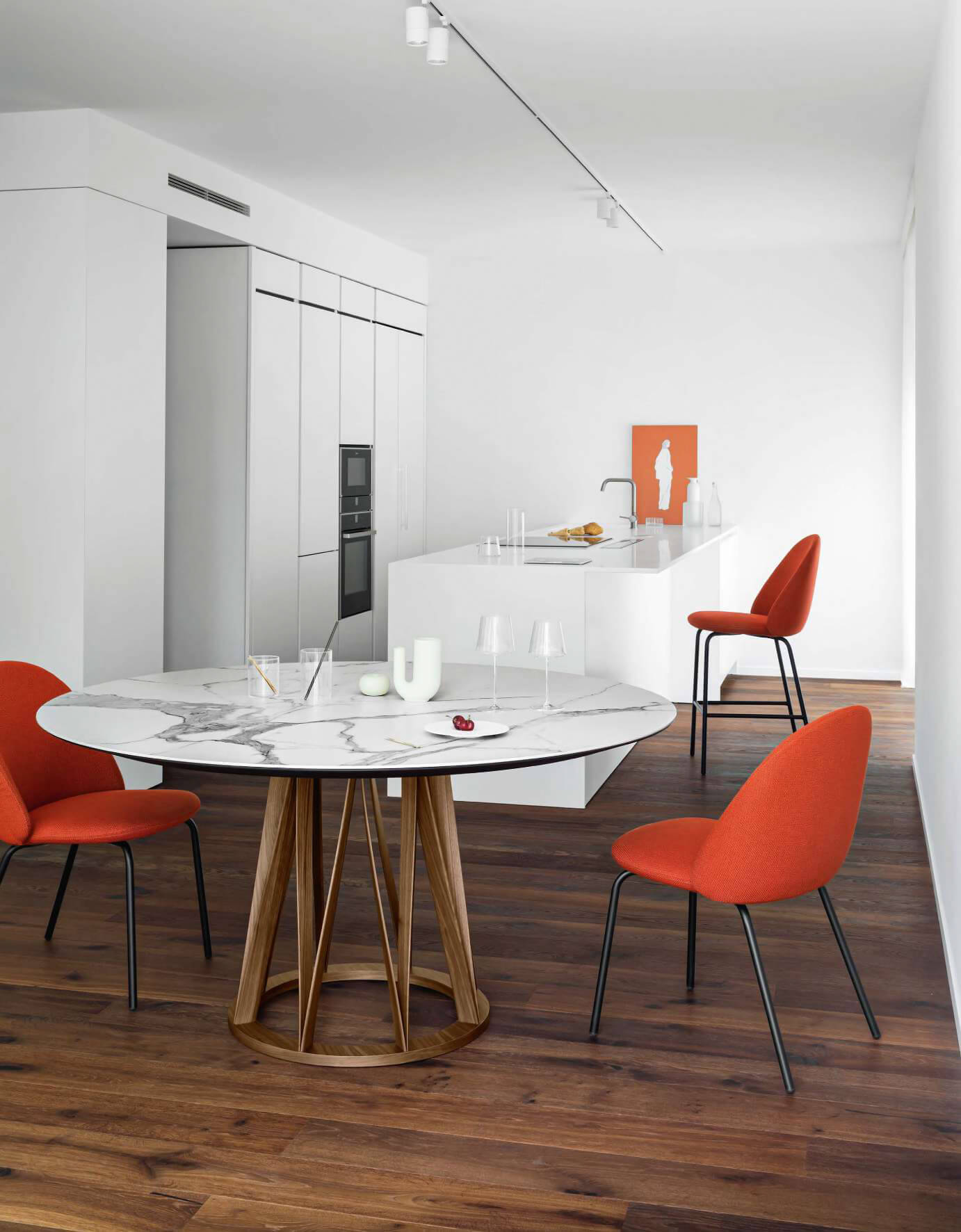 Round Acco table with white marble top and star-shaped light wood base, surrounded by four orange dining chairs in a minimalist interior.