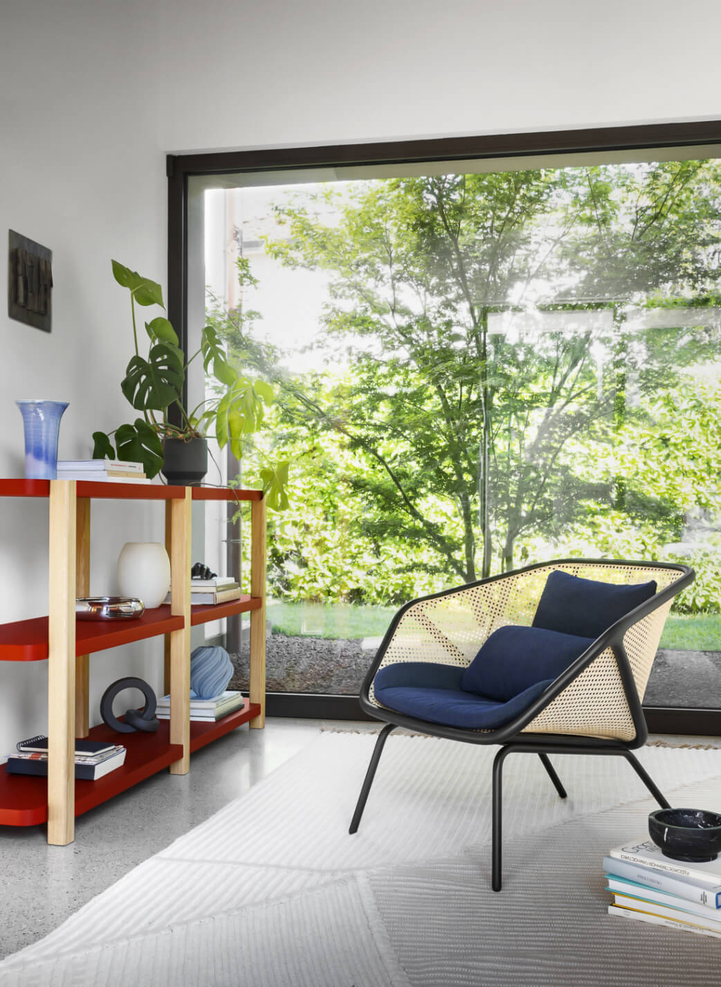 Colony lounge chair, black metal frame with woven rattan, navy cushion, positioned before glass door and red bookcase.