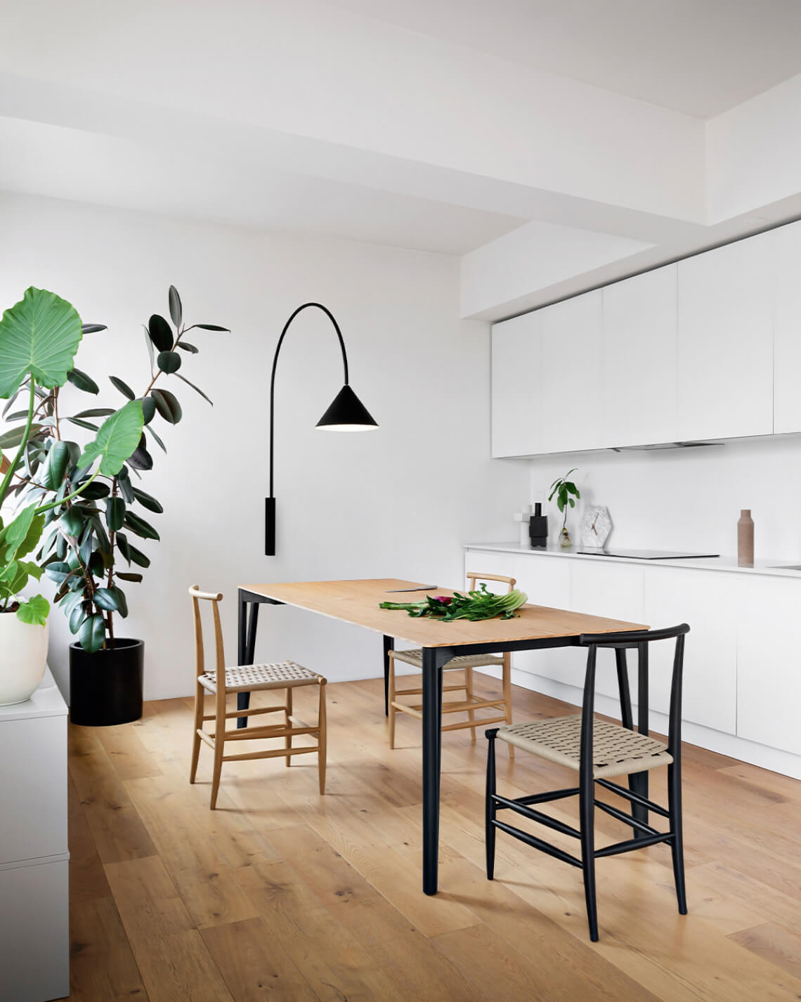 Miniforms Decapu Plus table, light wood top, black metal frame, paired with woven chairs in a white kitchen interior with plant decor.