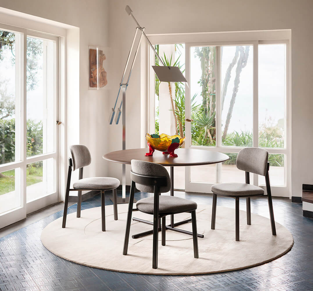 Potocco dining table, dark gray metal and top, with four gray fabric chairs on off-white rug in modern room with blue tile floor.