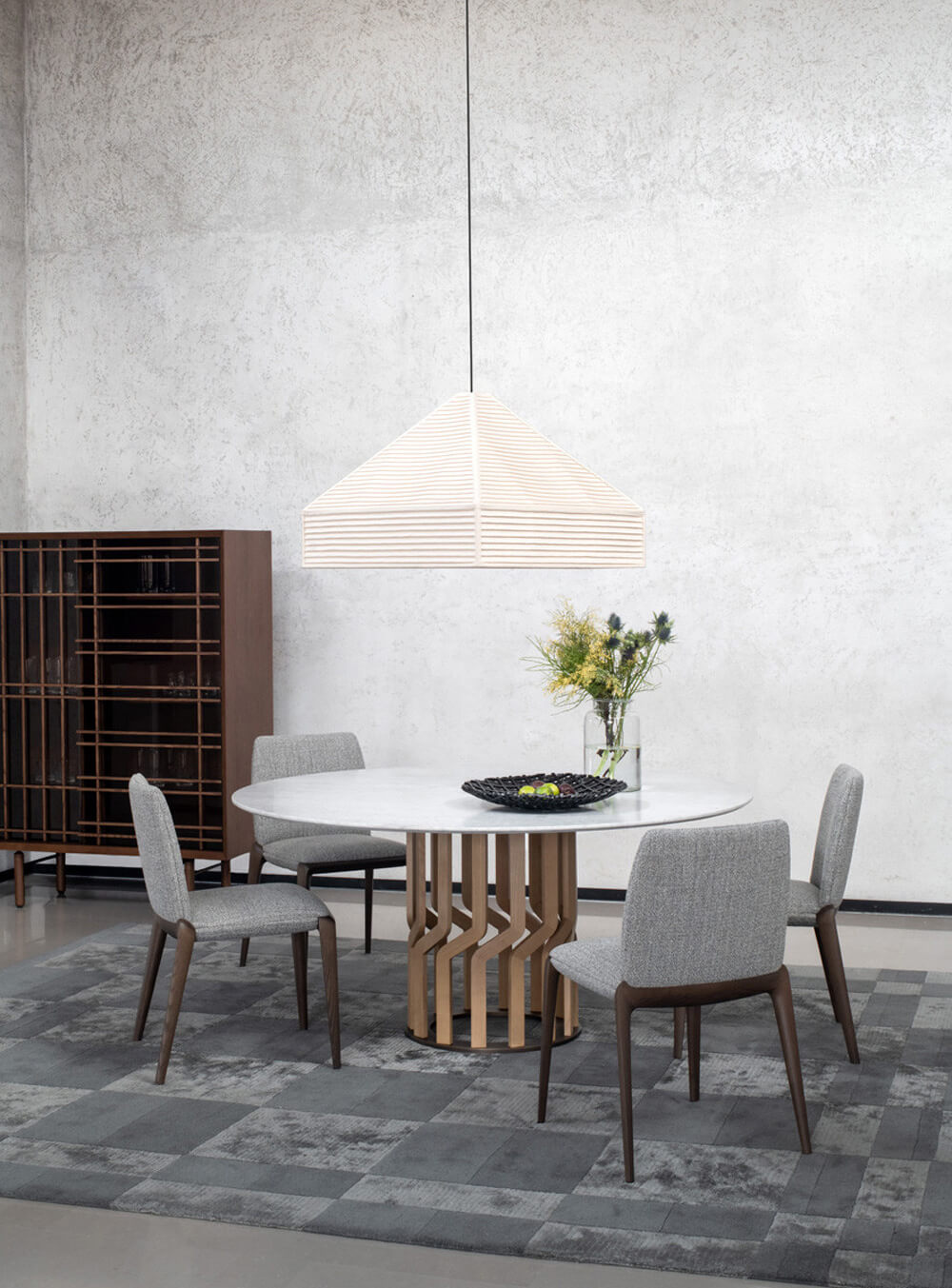 Round dining table with white marble top and brass interwoven base, surrounded by gray upholstered chairs in a modern interior.