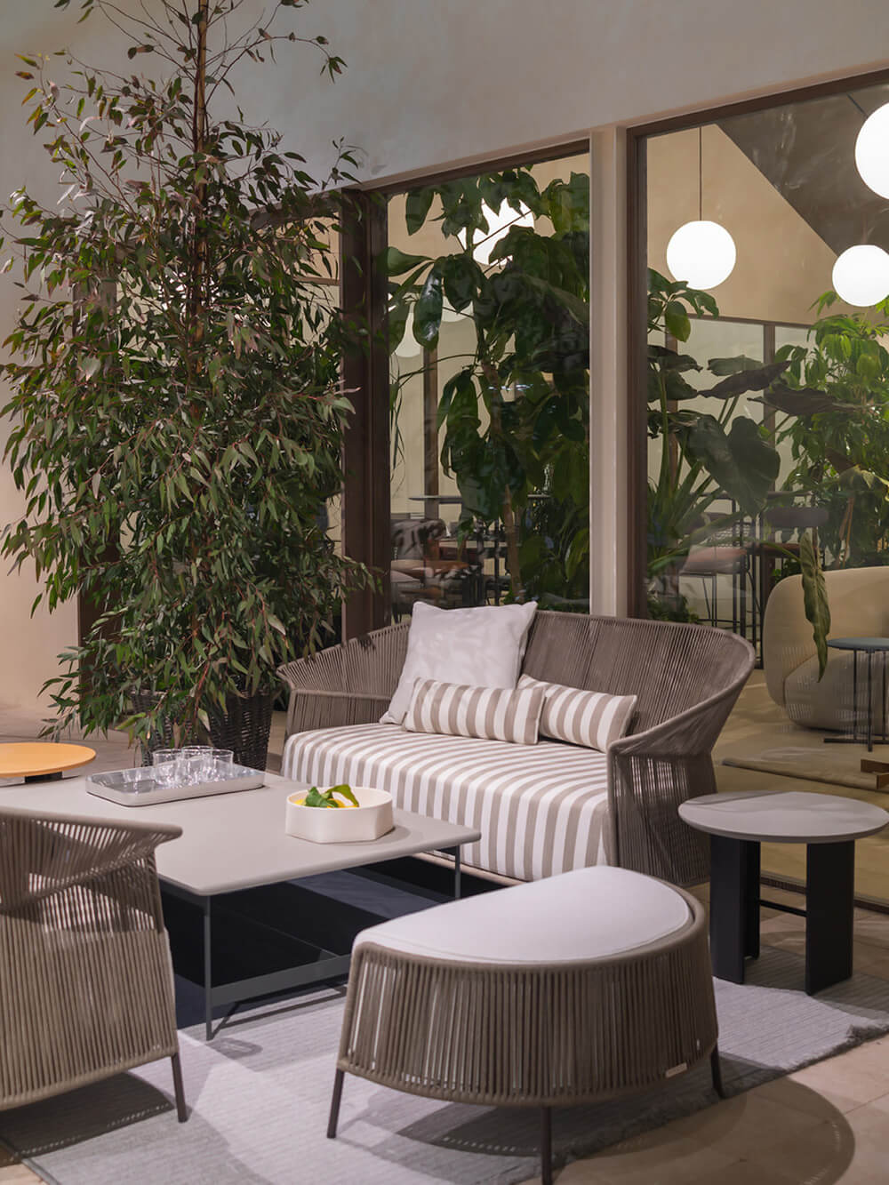 Potocco Ola sofa, gray woven cord, curved design with striped cushions, paired with ottomans and stone-top coffee table in outdoor setting.