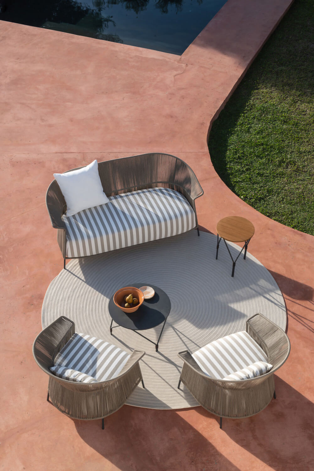 Potocco Ola sofa, woven dark brown frame, curved silhouette, gray and white striped cushions, terracotta patio, round gray rug.