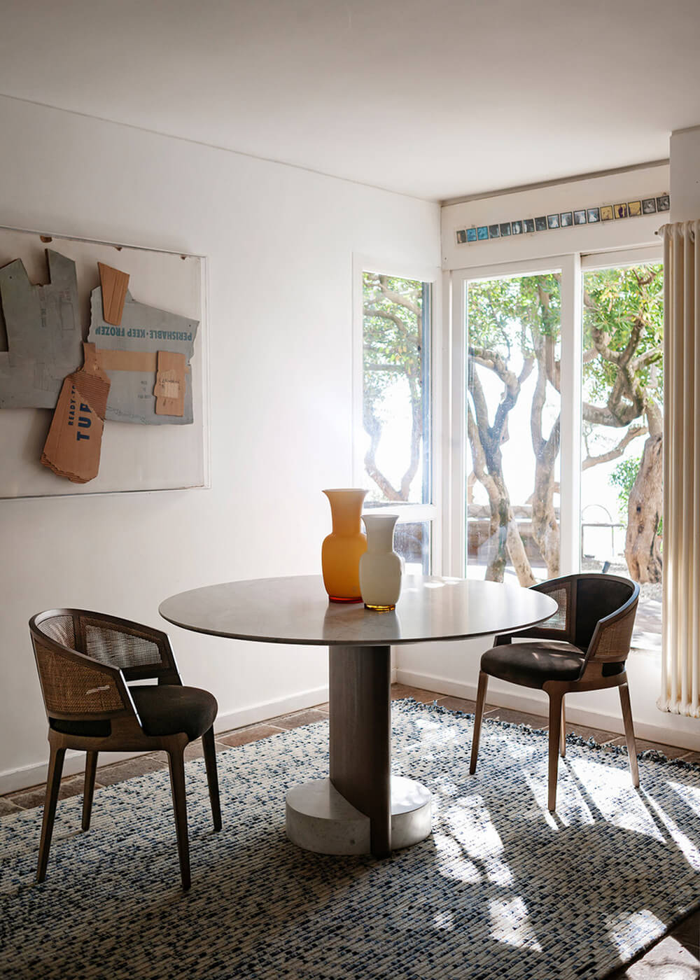Potocco Syn dining table, dark gray wood and concrete, round shape, paired with two gray upholstered chairs in a minimalist interior.