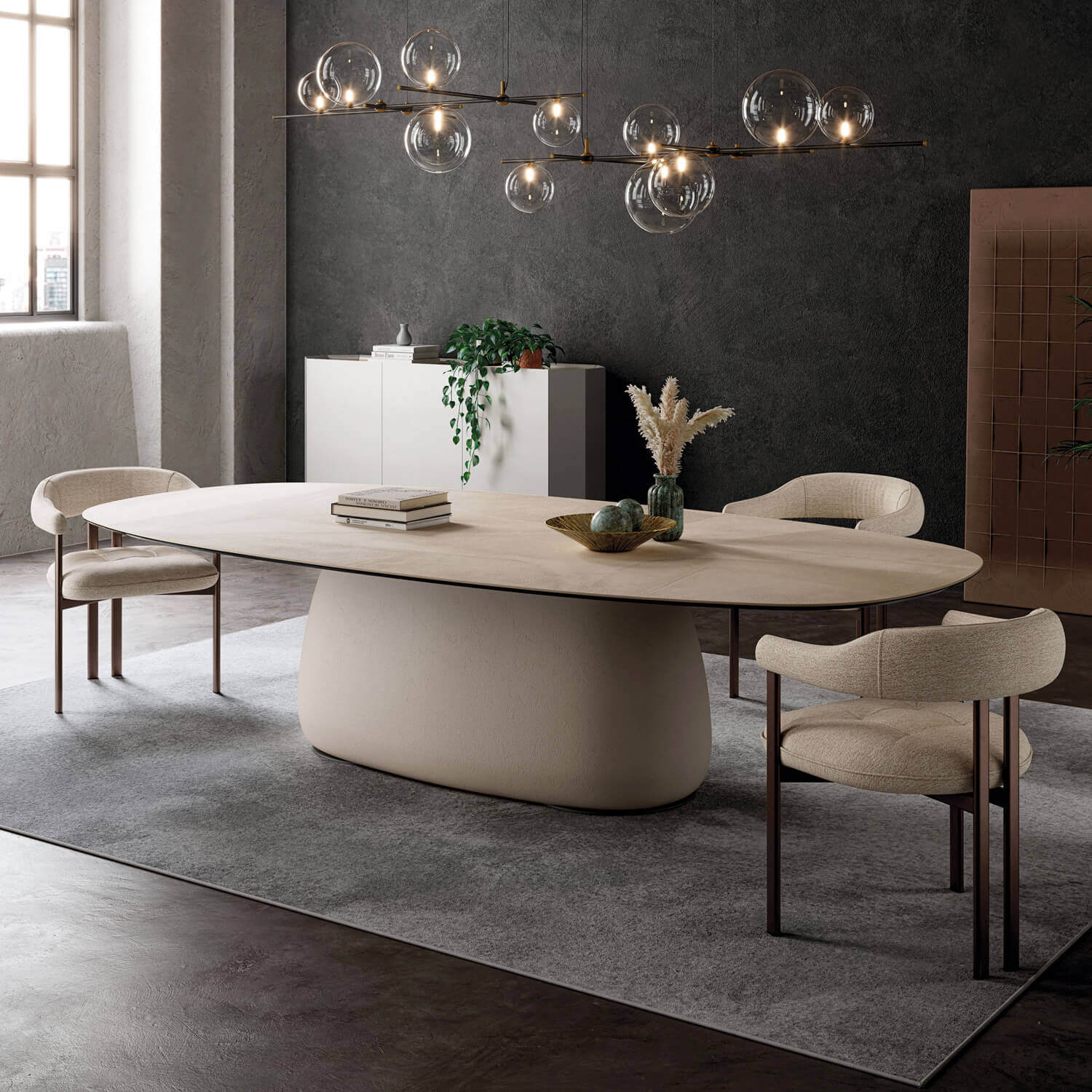 Oval dining table with beige textured top, curved base, and four beige fabric chairs with dark metal legs, under a glass orb chandelier.
