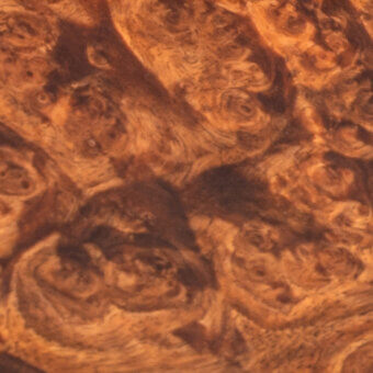 Radica wood texture displaying swirling brown and tan grain patterns, with polished surface and contrasting dark areas, showcasing dense organic forms.