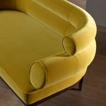 Bellavista Pyper sofa, mustard yellow velvet, rounded armrests with cylindrical bolster pillows and dark wood trim.