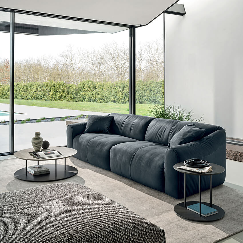 Modular sofa, dark gray leather, organic shape with rounded arms, paired with black metal side tables and a textured gray rug in a modern living room.