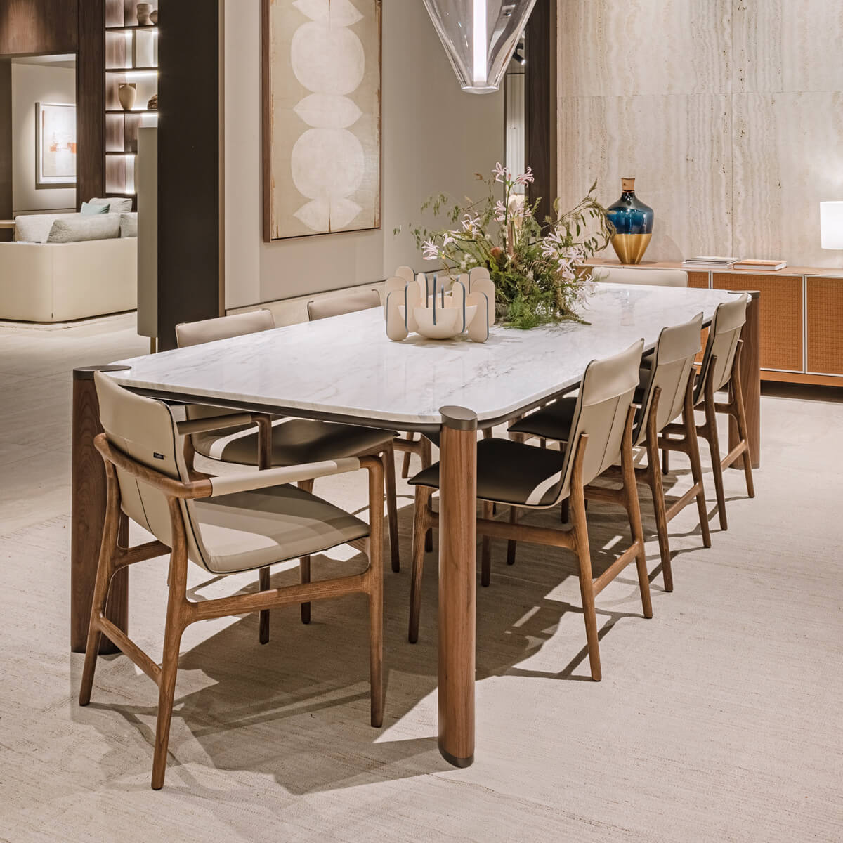 Marble dining table with walnut wood legs and mid-century modern chairs, featuring beige leather upholstery and a dried floral centerpiece.
