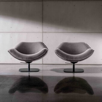 Alisia swivel lounge chairs by Sovet Italia, gray fabric upholstery, rounded biomorphic shape, black circular base, concrete block wall.