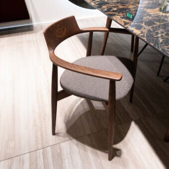 Xenial chair by Sovet Italia, gray fabric seat, walnut wood frame, curved armrests, four legs, marble table, beige tile floor.