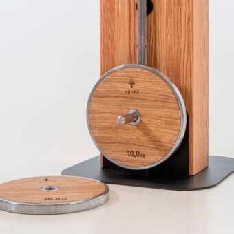 Weight plates, wood veneer, 10kg, displayed against white; black base supports circular forms, with NOHRD logo and vertical slat wood backdrop.