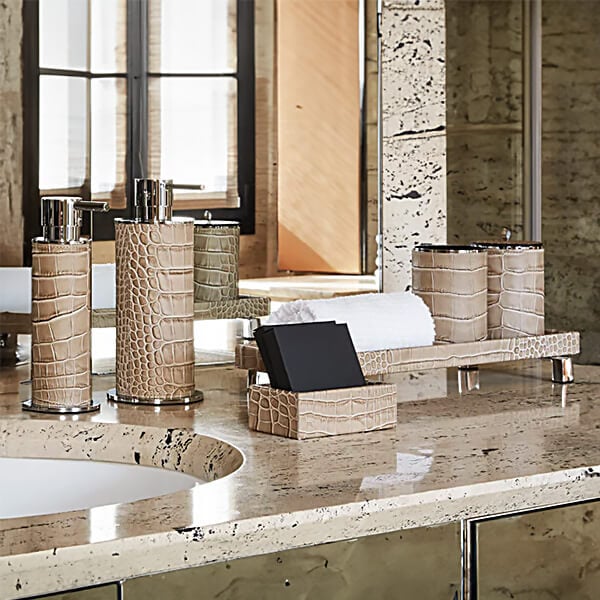 Beige & brown bathroom accessories on travertine marble: three textured cylindrical soap dispensers, towel tray, & square box.