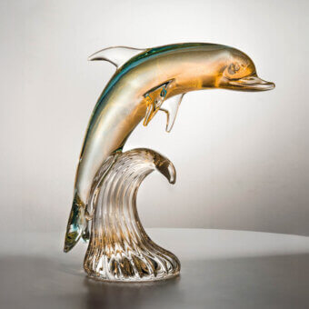 Glass dolphin sculpture, iridescent finish, leaping from stylized wave; teal, emerald, gold, amber gradient; translucent, blown glass form.