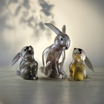 Glass rabbit sculptures by Duccio Di Segna, smoky gray and gold, detailed features, transparent forms on reflective surface.
