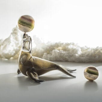 Bronze seal sculpture balancing a marbled sphere, reclining pose with textured finish, against a blurred cool-toned backdrop.
