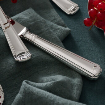 Schiavon cutlery set, stainless steel, stepped handles displayed on teal linen with red berries and floral patterned plate.