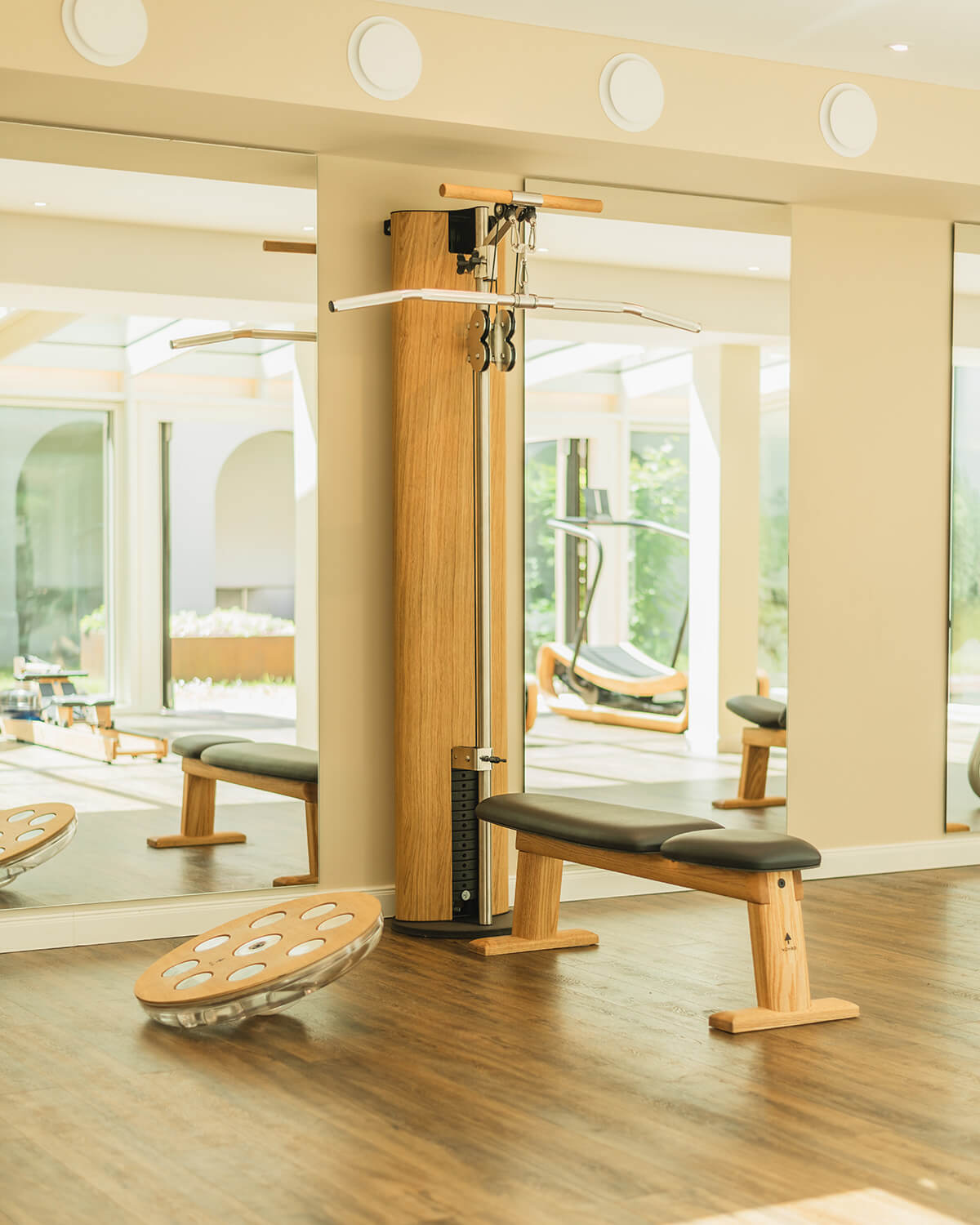 Waterrower Nohrd rowing machine with light wood frame, black bench, numbered increments, in a beige room with mirrored wall and fitness equipment.