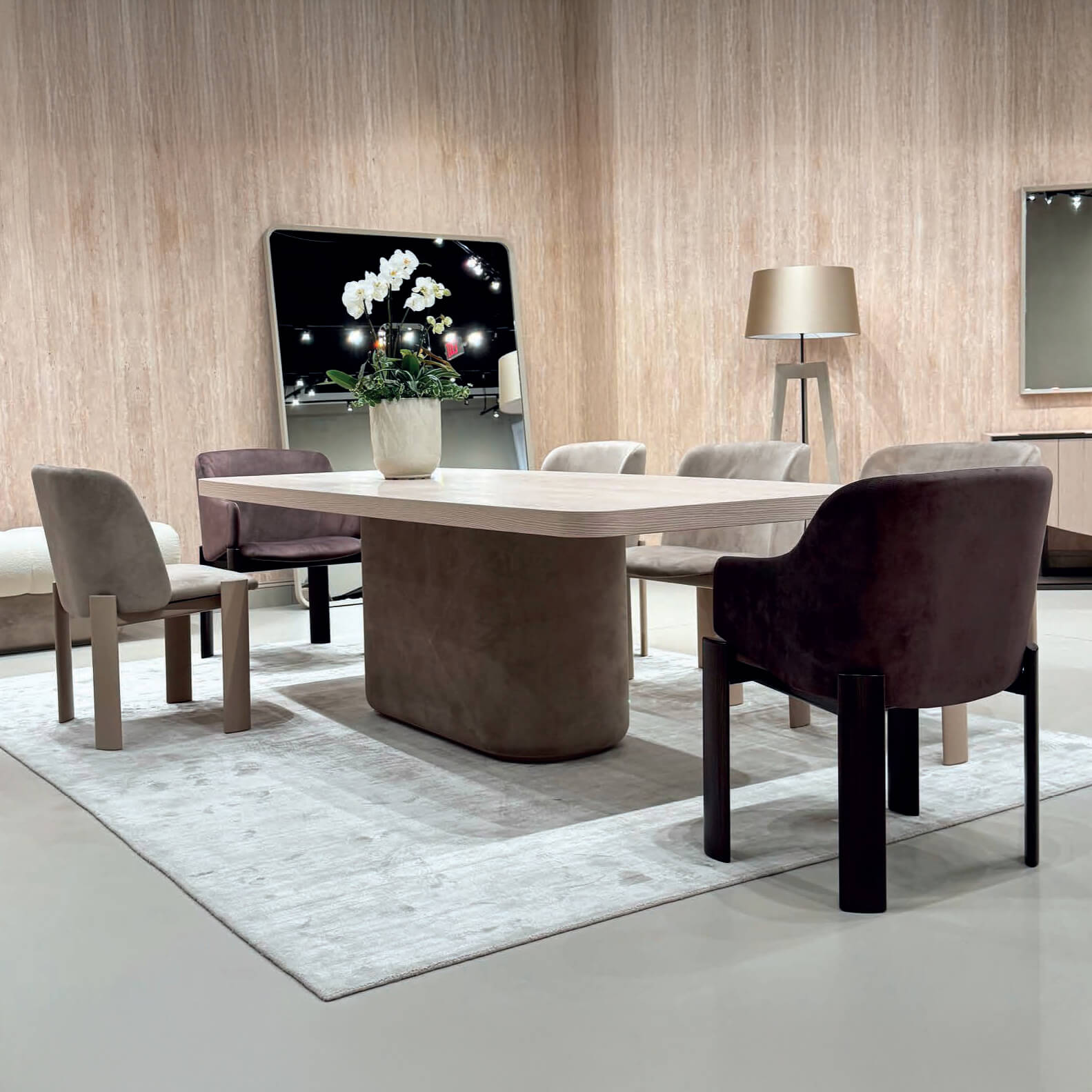 Dining room with wood table, four upholstered chairs, gray textured rug, wood paneled wall, gold lamp, orchids.