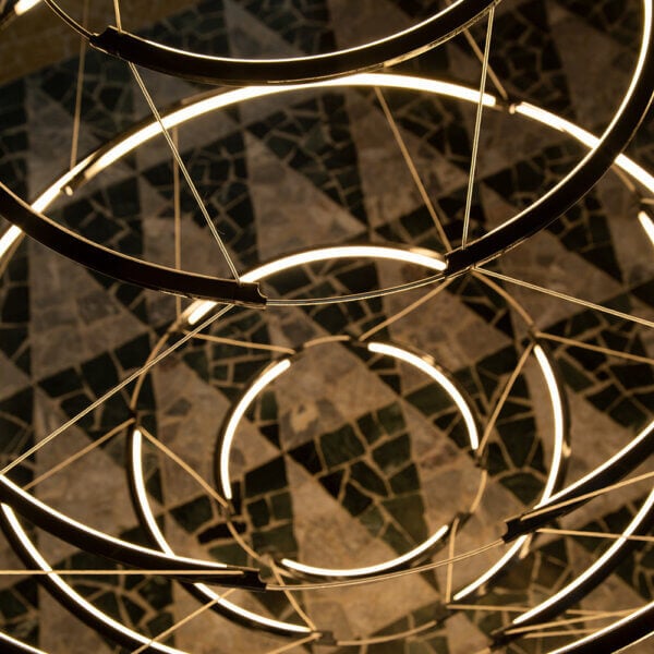 Concentric ring chandelier, dark metal finish, layered illumination above dark gray and beige mosaic tile surface.
