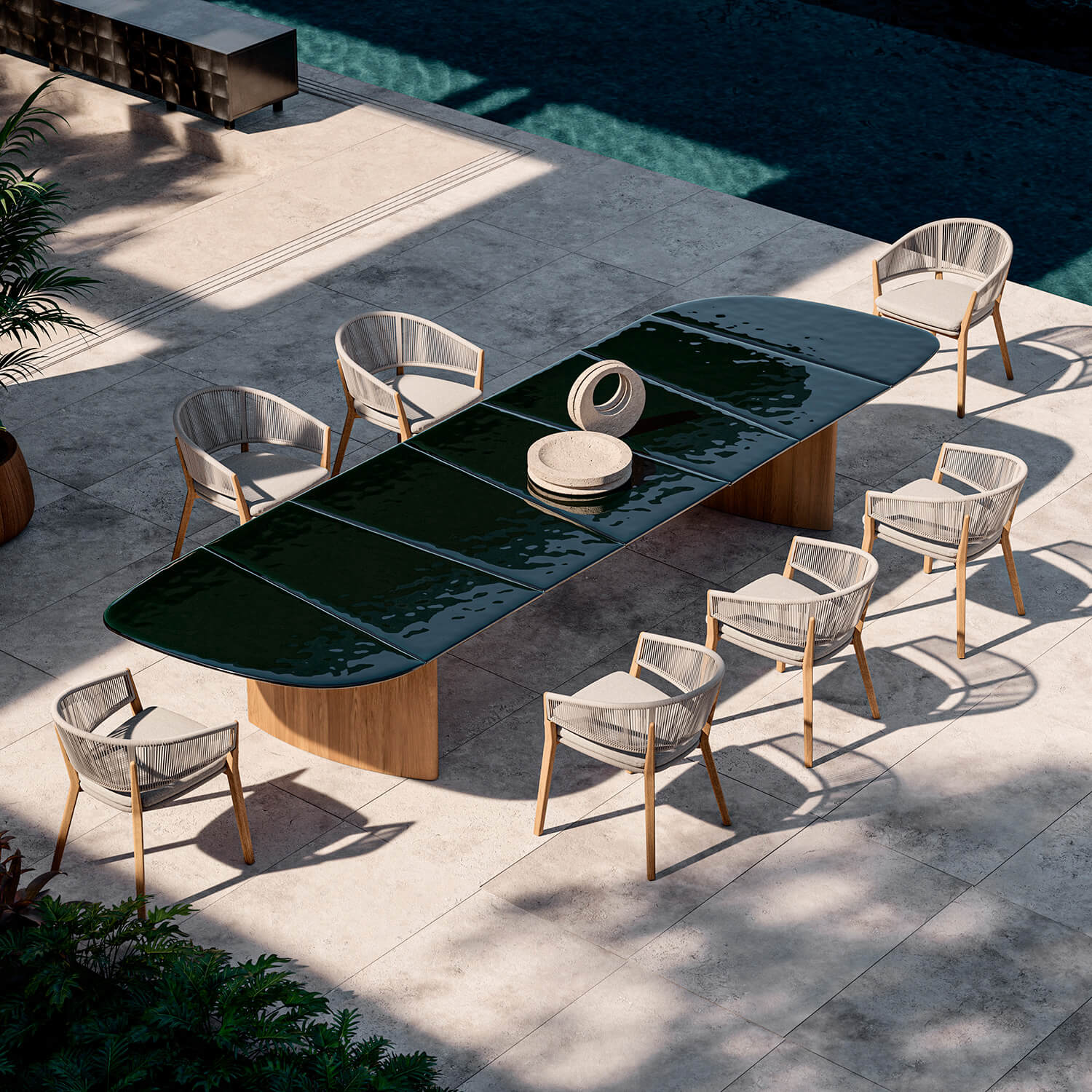 Oval dining table with dark green glass top and woven light gray chairs on a gray tiled patio near a teal pool.