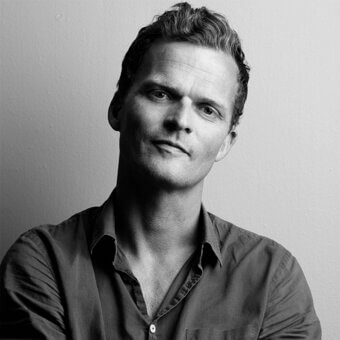 Black and white portrait of Andreas Engesvik, a man with dark hair wearing a button-down shirt, against a light gray wall.