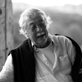 Black and white portrait of Ben Swildens, elderly man with white hair, glasses, and shawl, soft focus outdoor background.