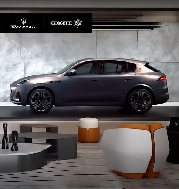 Dark grey Maserati Grecale SUV with black wheels, displayed with Giorgetti branding, marble table, and modern furniture against a textured grey wall.