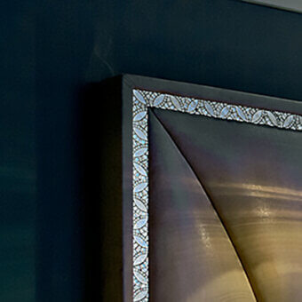 Mosaic frame detail with curvilinear tile pattern, dark wood and metallic border, layered golden-brown texture, teal background.